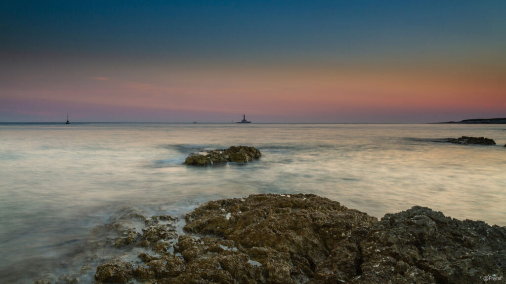 Meer bei Sonnenuntergang mit Felsen im Vordergrund.